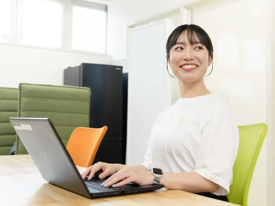 O.M.さん仕事風景。オフィスのテーブルでノートパソコンを操作している様子。