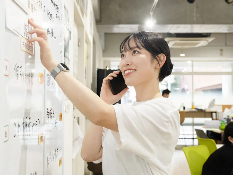 O.M.さん仕事風景。ホワイトボードを確認しながら電話対応している様子。