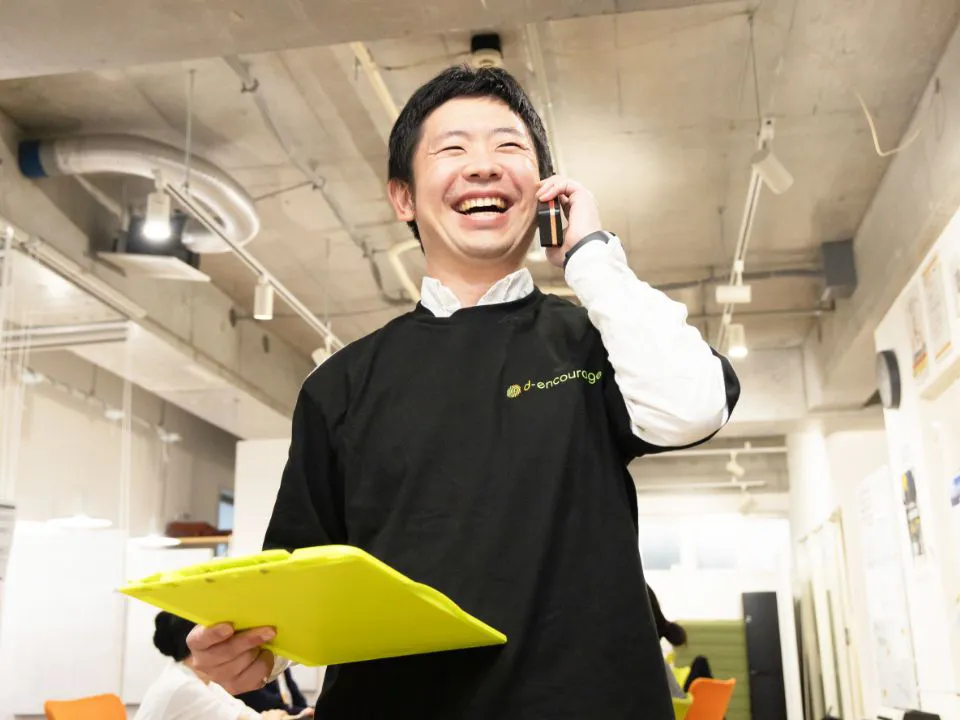 K.Y.さん仕事風景。クリップボードを持って電話をしている様子。