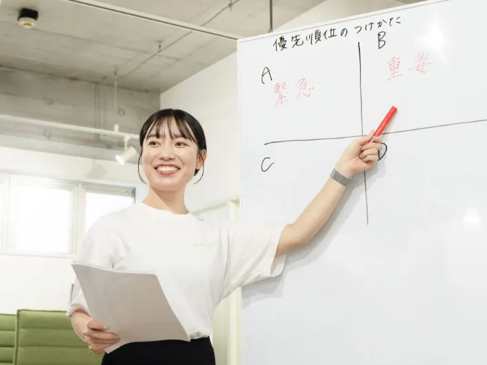 ホワイトボードを指しながら資料を持ち、座学の説明をしている様子。