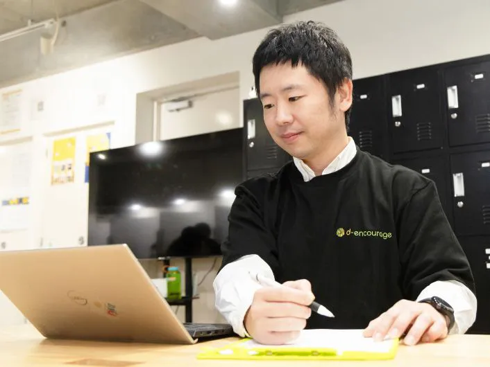 ノートパソコンと書類を前に、ペンを持って振り返りをしている様子。