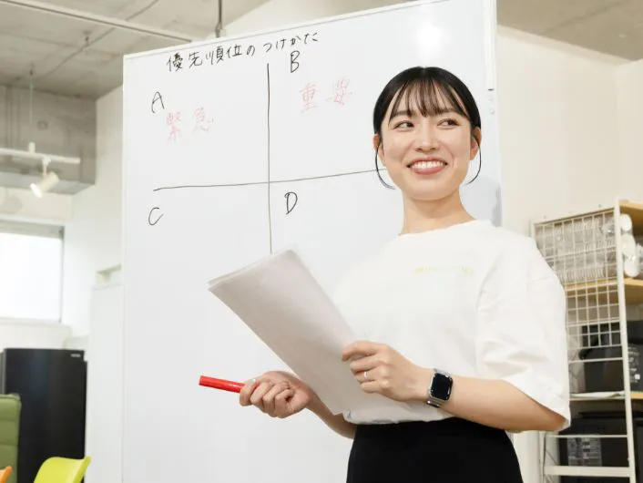 生活支援員の仕事風景1。ホワイトボード前で資料を持ち説明する様子。