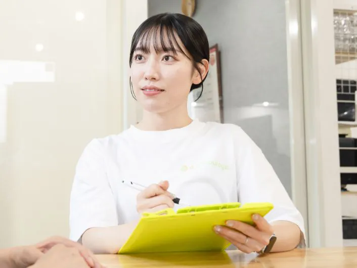 生活支援員の仕事風景3。ご利用者さまとテーブル越しに対話しながら、メモを取っている様子。