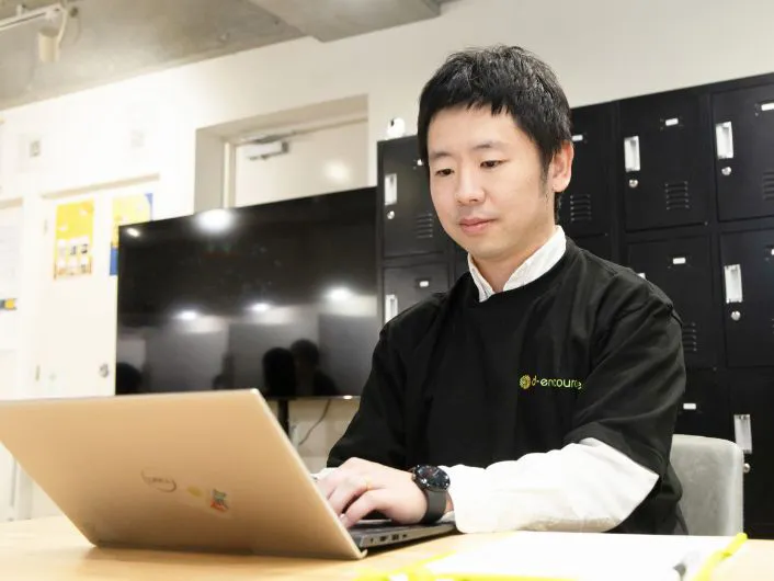 施設管理者の仕事風景2。オフィスでノートパソコンを使い、書類を手元に置いて事務作業をしている様子。