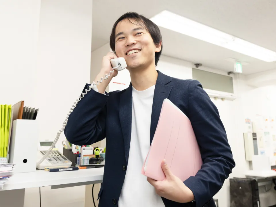 S.S.さん仕事風景。ピンクのファイルを持って電話対応をしている様子