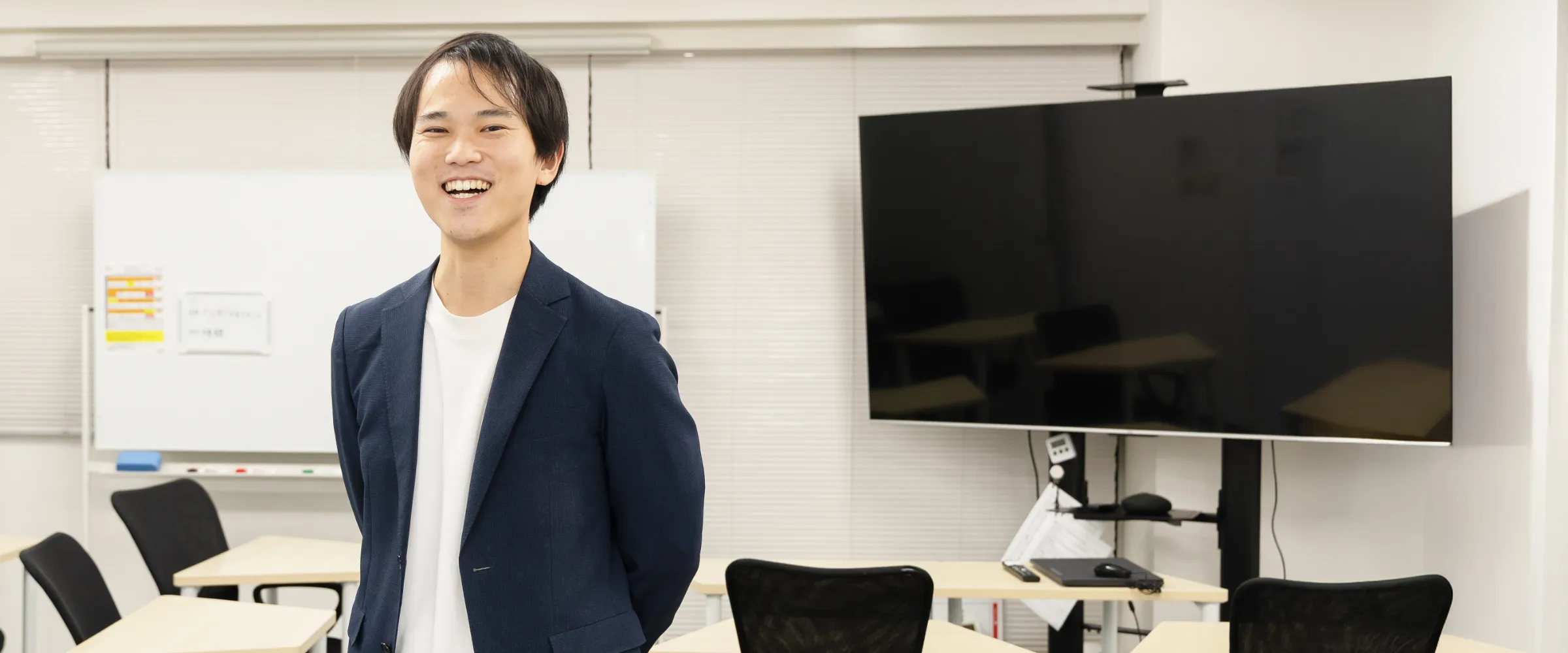 S.S.さんインタビューのキービジュアル。大型モニターとホワイトボードを背景に笑顔で立っている様子