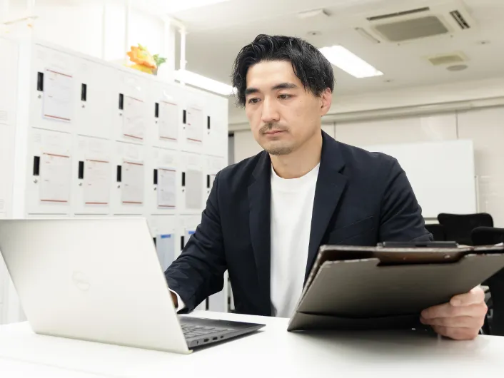 バインダーを片手にパソコン作業をしている様子