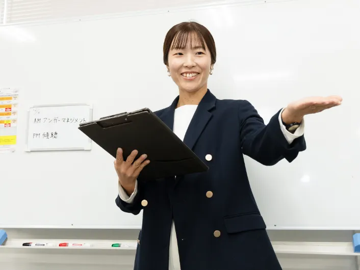 模擬会議でホワイトボードの前に立ち、バインダーを持って説明する職業指導員